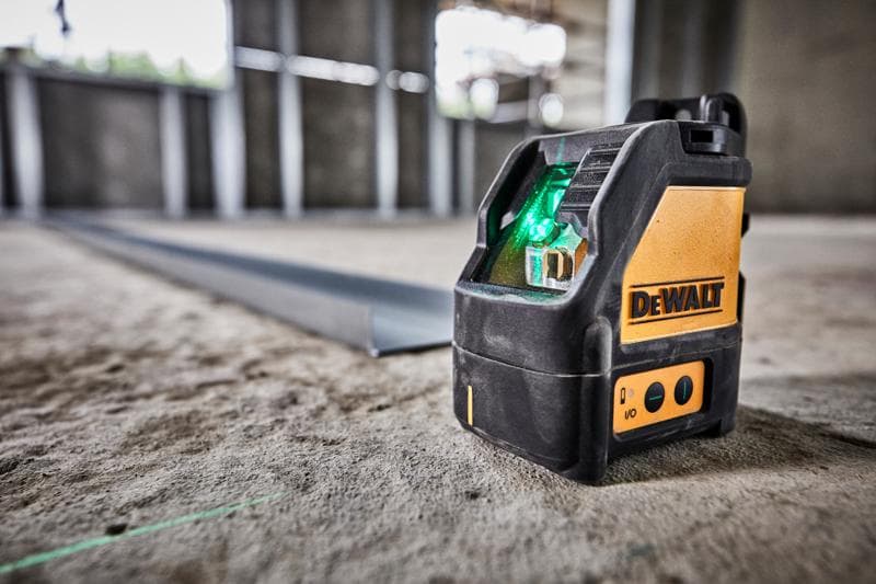 Nivel láser de haz verde DEWALT DW088CG sobre suelo de cemento en obra.